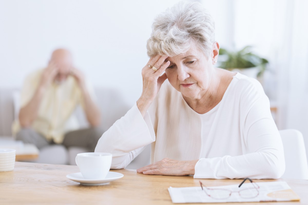 Eldre kvinne som holder seg for hodet på grunn av forverring av hjernens nevrologiske funksjoner, muligens Alzheimers sykdom. Eldre kvinne i forgrunnen med bøyd hode, støtter seg på hånden.