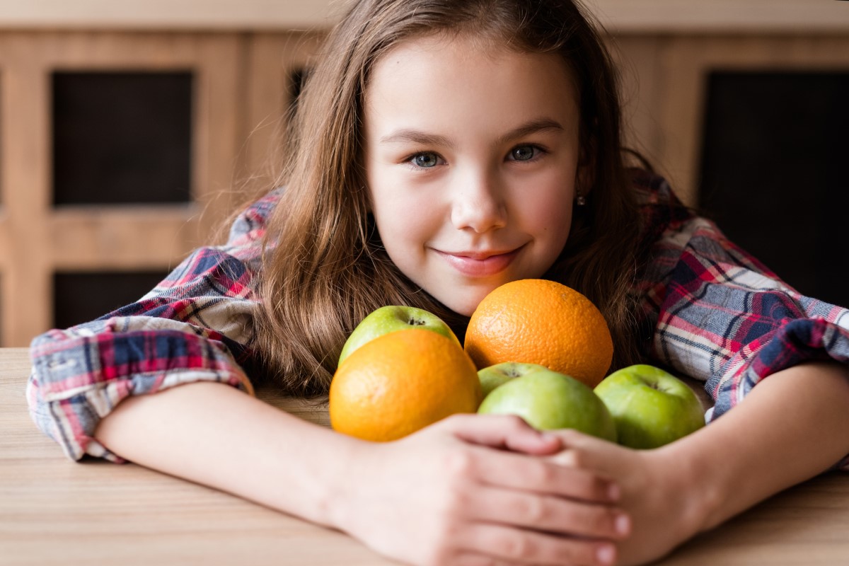 C-vitamin i frukt, et barn med appelsiner og epler i armene.