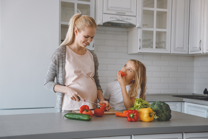 Gravid mor og datter tilbereder et sunt måltid på kjøkkenet.