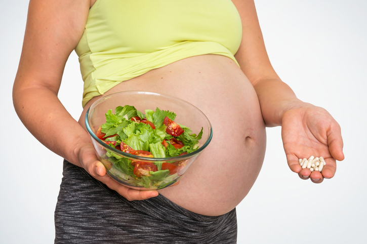 Gravid kvinne med salat og piller