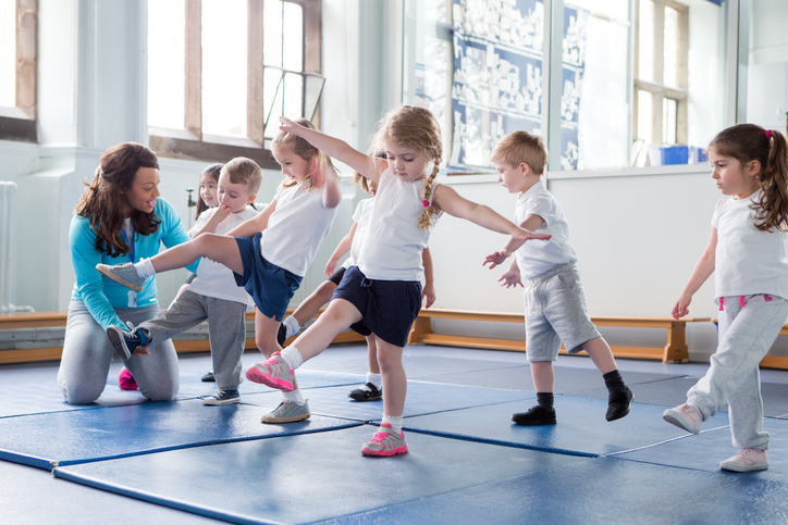 Små barn i gymsalen, der de øver sammen med læreren.