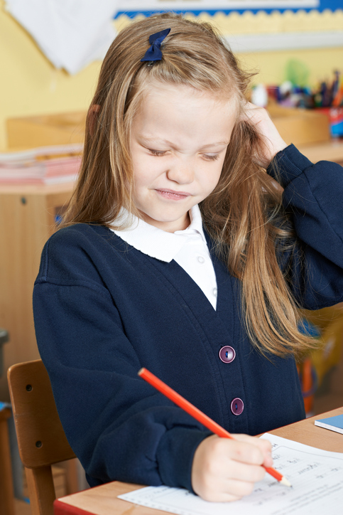 En liten jente som sitter på skolen med kløe i hodet, sannsynligvis lus i håret, blondt hår, sitter og skriver