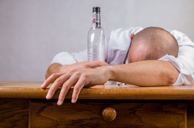 Alkoholisme er årsaken til humørsvingninger, en mann ligger på et bord med en tom flaske alkohol i hånden, en alkoholiker