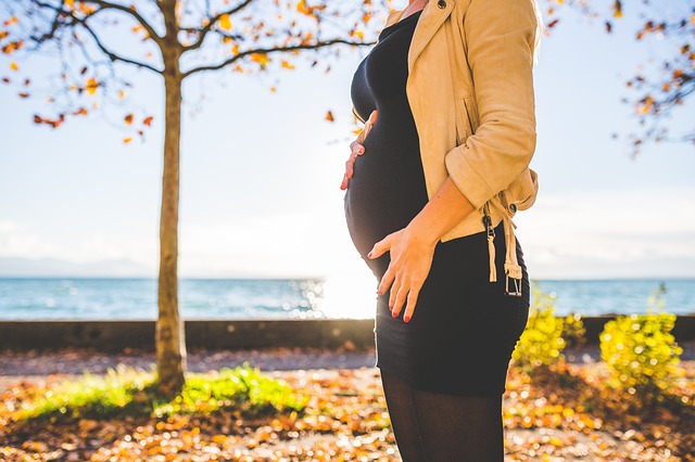 gravid kvinne står foran et tre om høsten